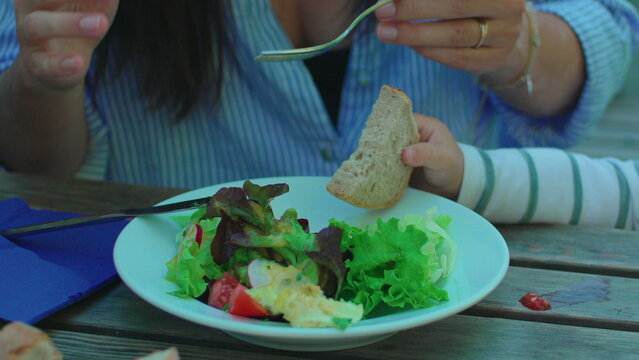 Parent serving bread beside fresh salad during outdoor family meal capturing healthy eating, caregiving and authentic casual dining lifestyle