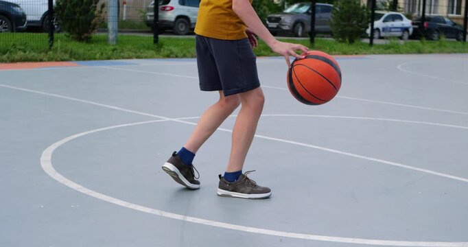 Young boy learns to dribble basketball on outdoor court during sunny summer day. Child practices ball control and coordination while enjoying recreational sports activity on playground