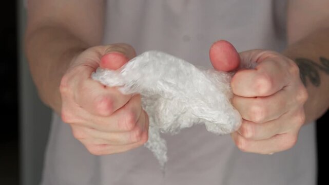 A man crumples a plastic bag with bubbles in his hands.