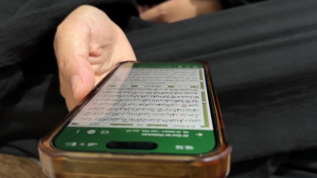 Muslim woman reading digital Al Quran on smartphone screen at home