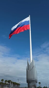 Russian flag waving on a tall flagpole with an elaborate metal base, showcasing national identity and sovereignty under a clear sky with scattered clouds