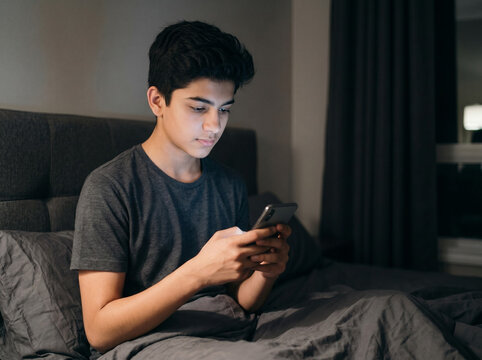 16 year old indian teenage boy using smartphone at night in bedroom representing social media addiction screen time insomnia online communication and digital wellness awareness
