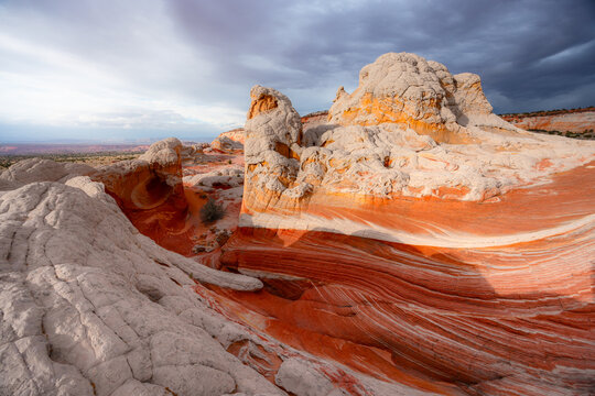 View of the unique White Pocket sandstone formations with swirling red layers and white textures under dramatic storm clouds in Coconino County, Arizona, United States.
