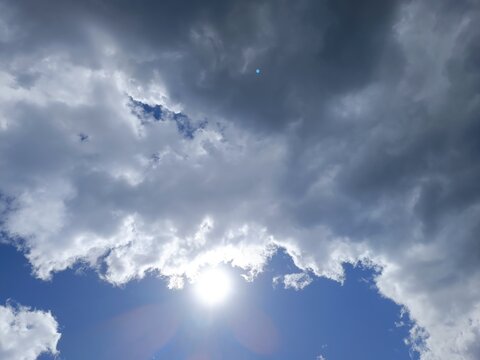 Bright sun emerging from behind dark grey storm clouds. Dramatic weather background with blue sky