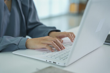 Fototapeta premium A person types on a white laptop keyboard while sitting at a desk.