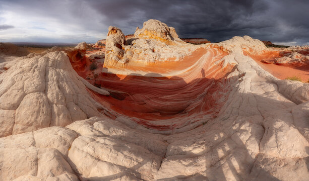 View of the swirling white and orange sandstone formations of White Pocket with shadows of people under dramatic storm clouds in Coconino County, Arizona, United States.
