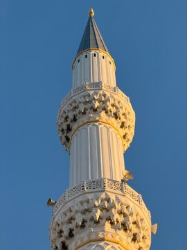 View of a tall white minaret with intricate stone carvings and loudspeakers against a clear blue sky in Besiktas, Istanbul, Turkiye.