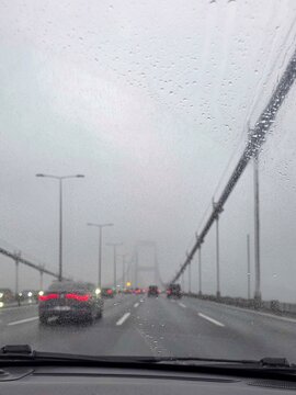View of cars driving on a suspension bridge during a rainy day with raindrops on the windshield in Besiktas, Istanbul, Turkey.