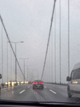 View of cars driving across a suspension bridge through a rainy windshield with wet asphalt and overcast sky in Besiktas, Istanbul, Turkey.