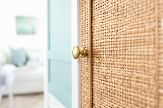Woven cabinet door with brass knob and soft blurred living room background