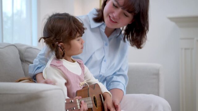 Little girl confidently playing the ukulele while her mother applauds