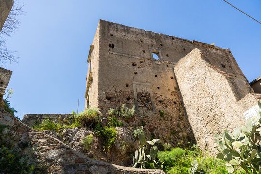 View of the Castello di Pentefur ruins with weathered stone walls and small square openings under a clear blue sky in Savoca, Sicily, Italy.