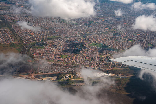Aerial view from an airplane window shows Johannesburg suburbs, grid streets, cul de sacs, small parks, larger facilities, and the wingtip under soft daylight.