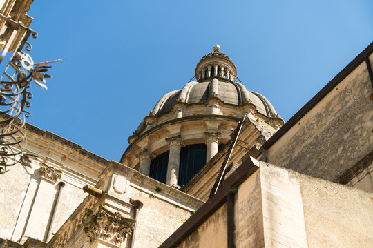 View of the ornate baroque dome of the Cathedral of San Giorgio with stone columns and architectural details under a clear blue sky in Ragusa, Sicily, Italy.