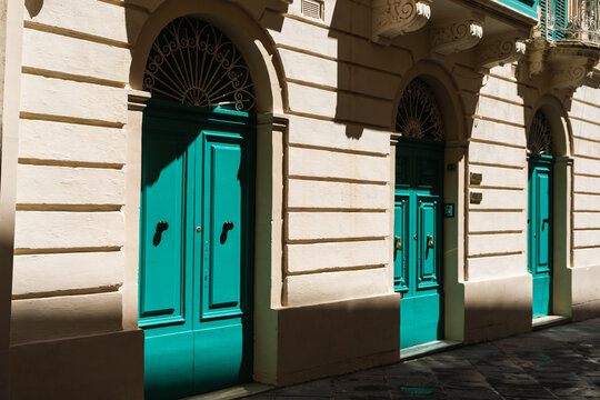 View of traditional turquoise wooden doors on a limestone building with arched fanlights and decorative stonework in Rabat, Western Region, Malta.