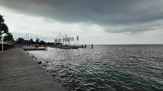 Bardolino, Italy - May 14, 2026 - Sailboats docked at a marina on a cloudy day with rippling water and wooden pier
