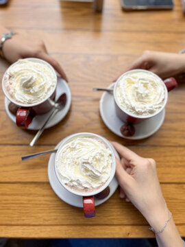View of three mugs of hot chocolate topped with whipped cream on a wooden table with hands of people Beylikduzu, Istanbul, Turkiye.
