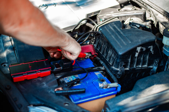 Connecting a portable jump starter to a car battery under the hood. vehicle maintenance, roadside assistance, emergency car start.
