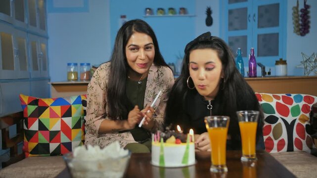 Teenage girl blowing candles on the cake and celebrating her birthday at home. Birthday celebration in social distancing during Coronavirus - Mother-daughter making an online video call on a specia...