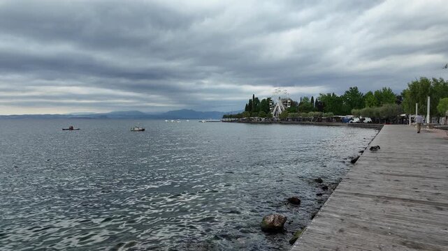 Bardolino, Italy - May 14, 2026 - Scenic lakefront with a Ferris wheel and boats on a cloudy day