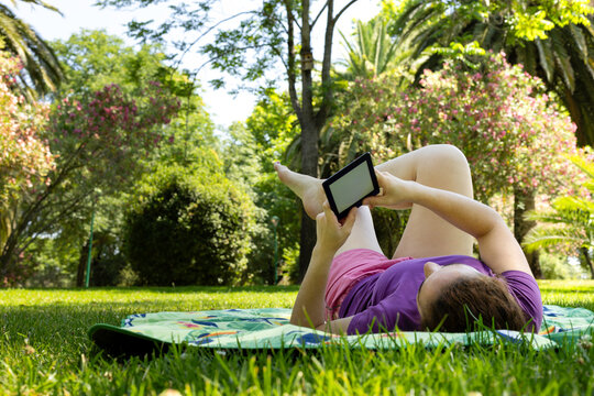 A woman lying on her back while reading an e-book
