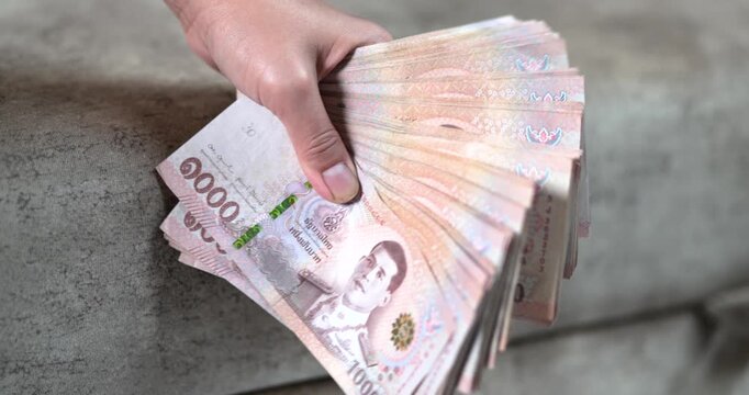 Hand holding Thai baht banknotes, money, cash, representing finance, salary, savings, investment, business, cash flow, and everyday economy concepts