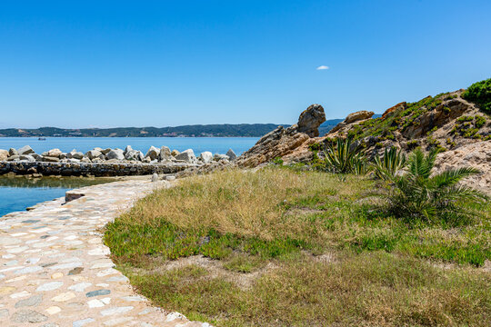Stone path that leads to a beach with a boat in the water, Ammoulliani, Greece