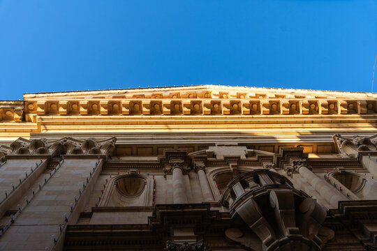 View of the ornate baroque facade of a historic building with stone carvings and columns under a clear blue sky in Valletta, Port Region, Malta.
