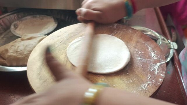 Indian woman rolling a fresh dough ball to make traditional roti (chapati) on a wooden board