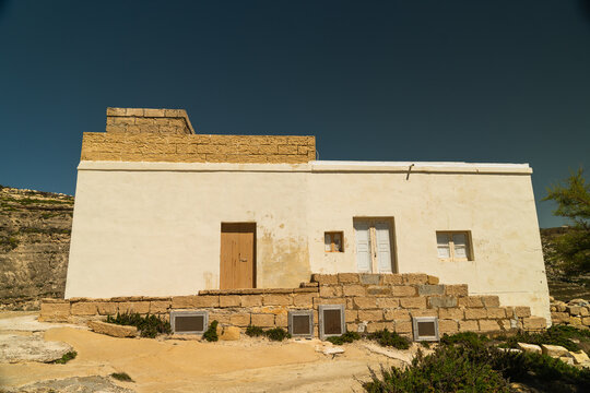 View of a traditional white stone building with stone steps and wooden doors near Dwejra Bay in Zebbug, Gozo Region, Malta.