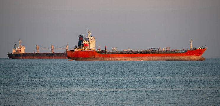 Large oil tanker and cargo ships navigating through the blue ocean, representing global maritime trade and shipping logistics in the Strait of Hormuz.