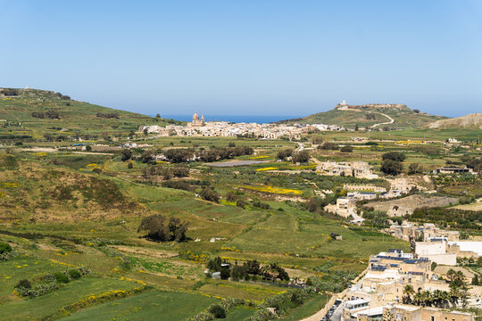 View of the town of Zebbug with its parish church dome overlooking terraced green fields and the Mediterranean Sea in Zebbug, Gozo Region, Malta.