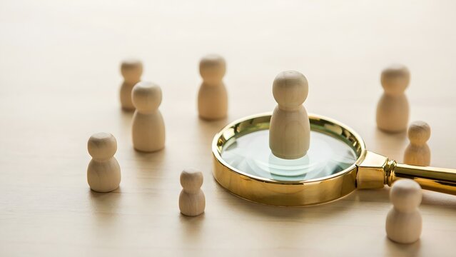 Magnifying glass focusing on one wooden figure from a group, representing talent identification, strategic selection, and finding the right individual for business, recruitment, and leadership