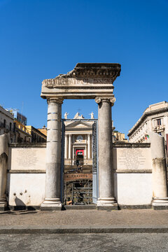 View of the ancient Roman columns and ruins of the amphitheatre with a historic church facade in the background under a clear blue sky in Catania, Sicily, Italy.