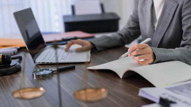 professional lawyer working at office desk writing legal documents using laptop computer with gavel and magnifying glass for justice legal consultation