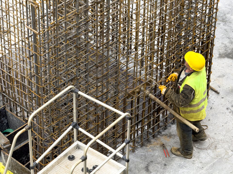 View of a construction worker in a yellow hard hat and safety vest working on a steel rebar structure at a building site in Avcilar, Istanbul, Turkiye.