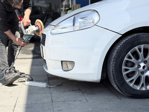 View of a man using a rotary polisher to buff the front bumper of a white car at a detailing shop in Avcilar, Istanbul, Turkiye.