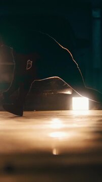 Silhouette of a young stylish guy freerunner doing a series of jumps, flips, and turns in the garage in front of car's headlights