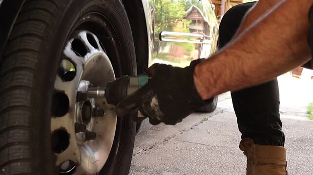 Detailed view of a mechanic aligning a cordless impact wrench with a wheel lug nut during vehicle service. Professional automotive maintenance and repair work in progress.
