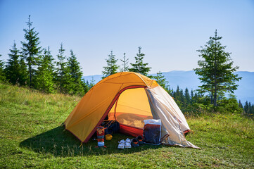 Bright yellow tent with camping gear on grassy hillside, overlooking breathtaking panorama of...