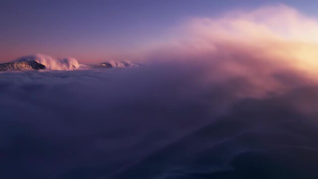Aerial perspective of clouds forming large cresting ocean waves with curling barrels, illuminated by warm golden sunlight and purple atmospheric tones during sunset.