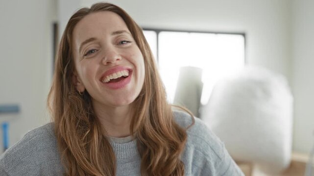 Woman laughing with mouth open amid moving boxes and bubblewrap, smiling in a sunlit building interior while unpacking; happiness warmth.