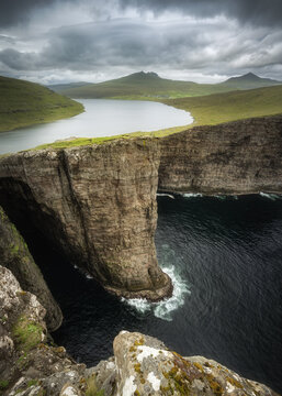 View of the dramatic Traelanipa cliffs and Lake Sorvagsvatn overlooking the dark Atlantic Ocean under a heavy cloudy sky in Vagar, Vagar, Faroe Islands.