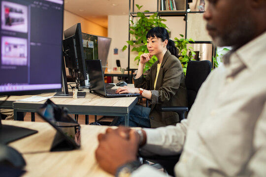 Businesswoman working at laptop with coworker in modern office