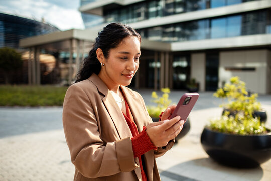 Businesswoman using smartphone outside modern office building