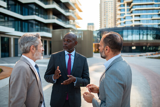 Three businessmen discussing strategy outside modern office complex