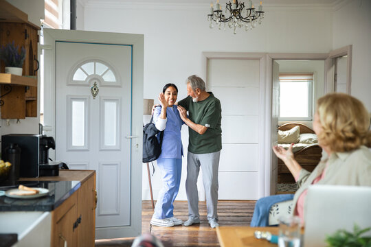 Caregiver waving goodbye to senior couple at home