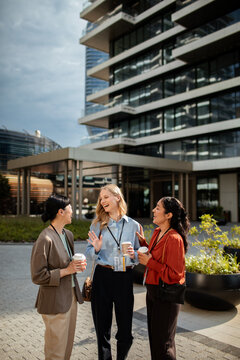Three businesswomen networking with coffee outside a modern office building