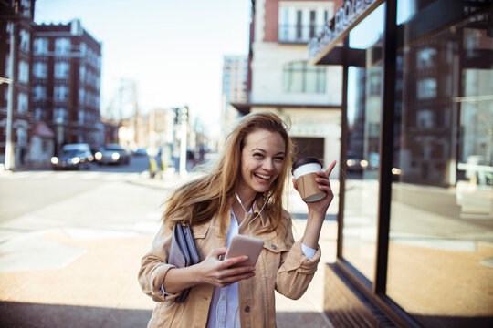 Smiling young woman with coffee and smartphone on city street