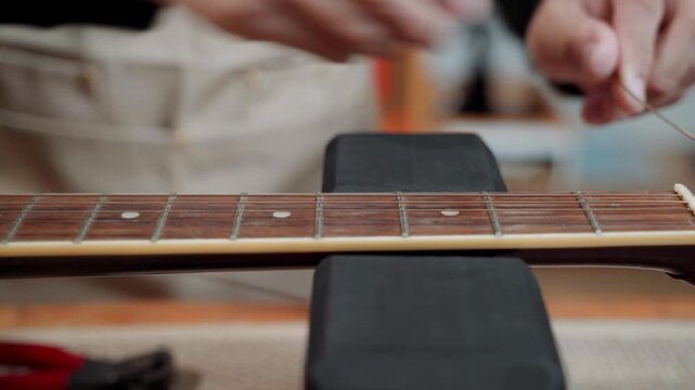 Close-up of a professional guitar technician cutting and removing old guitar strings before restringing an electric guitar. Instrument maintenance and repair process in a music workshop.
